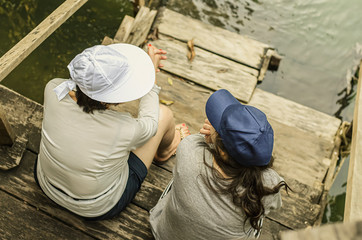 Top view of two womens having a conversation, seated side by side on a wooden deck next to the river bank. Mother and daughter relationship.