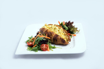 A low contrast image of a breakfast platter with egg-filled croissant with vegetables- carrot, tomato, lettuce on a minimal white background with a 30 degree angle from front perspective