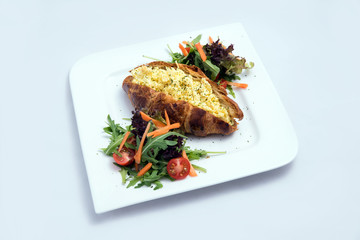 A low contrast image of a breakfast platter with egg-filled croissant with vegetables- carrot, tomato, lettuce on a minimal white background with a 30 degree angle from front perspective