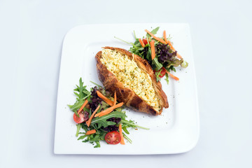 A low contrast image of a breakfast platter with egg-filled croissant with vegetables- carrot, tomato, lettuce on a minimal white background with a 30 degree angle from front perspective