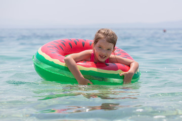 Fototapeta na wymiar happy little girl is swimming in an inflatable circle in the sea, Adriatic Sea, Croatia