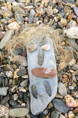 Simpatic face created on a beach with small stones and dried algae