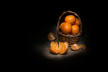 Basket with mandarins and peeled tangerine slices, still life on black background