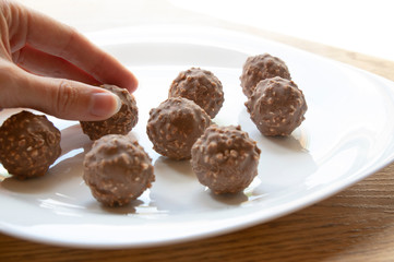 female hand tries round chocolate candy with nuts on a white plate