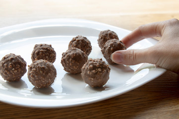 female hand tries round chocolate candy with nuts on a white plate