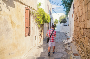 Fototapeta na wymiar Tourist walking around the old town of Lindos in Rhodes, Greece. Typical narrow lanes and white houses in Greece. Enjoy summer holidays traveling around Europe.