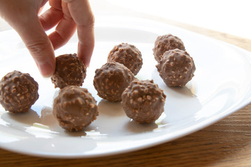 female hand tries round chocolate candy with nuts on a white plate