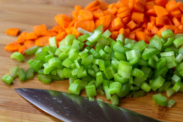 Close up on diced up carrots and celery on a cutting board with a knife