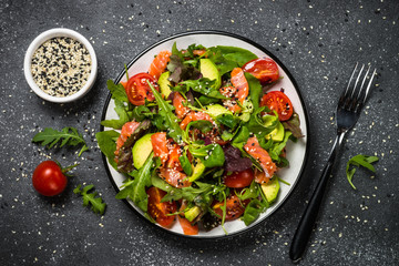 Salmon salad with fresh vegetables on black top view.