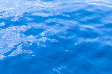 The background or texture of the blue water surface of the river, lake or sea with the waves, ripples and flares