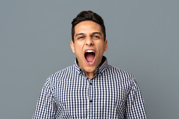 Young man screaming loudly at camera on gray background