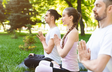 Three friends holding hands in namaste while practicing yoga outdoors