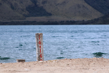 A pole with a number written in red next to the water with mountains in the background