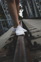 Female legs to the knees, in white sneakers, stand on the rails. There is a place for text. Copy space.