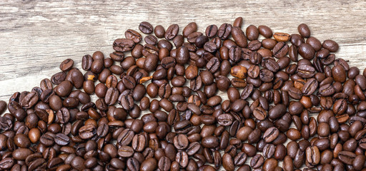 Roasted coffee beans, on a wooden surface.