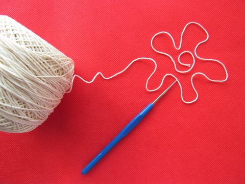 Hobby, crochet. Crochet hook and a ball of white thread. The thread is folded in the form of a flower.