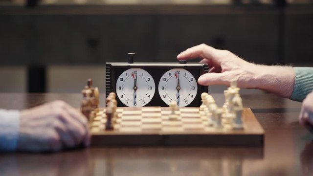 cropped view of two senior men playing chess and pressing button on chess clock at table 