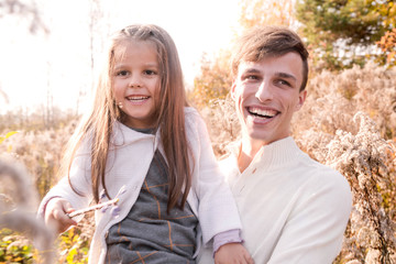 Happy dad and daughter posing among autumn yellow dry plants