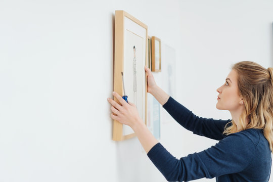 Young woman hanging a picture on a wall