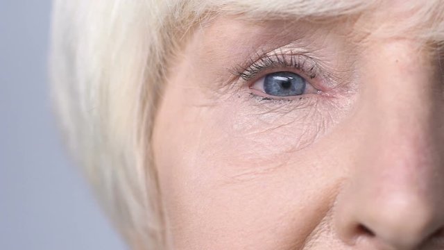Old woman with red eyes looking into camera, allergy to cosmetics, lacrimation