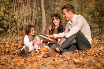 Family picnic in the autumn park. Family drinking tea