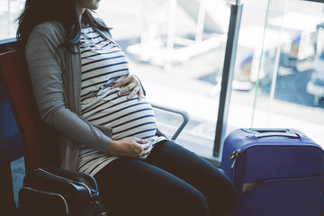 pregnant women sit holding their stomach in the airport waiting room before departure
