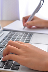 Side view of accountant's hands doing paperwork on cork desktop and laptop keyboard