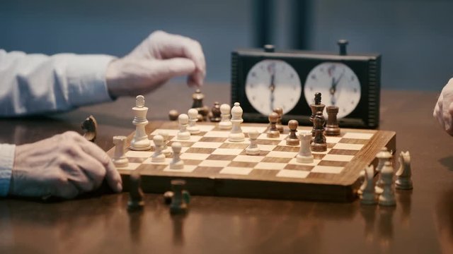 cropped view of two senior men playing chess and pressing button on chess clock