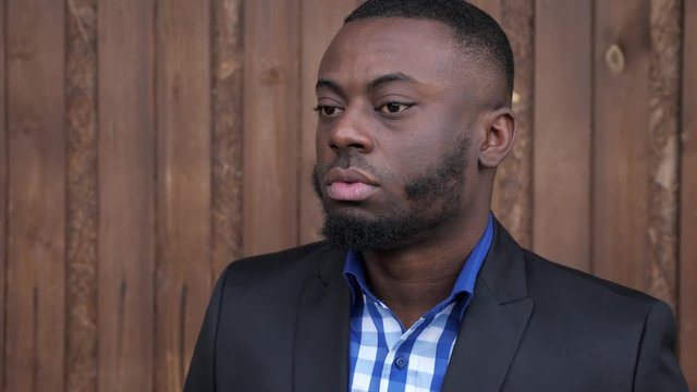 Portrait of young black bearded guy looking at camera. Afro american man in suit is turning gead and smiling. He is happy and confident.