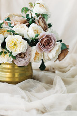 Flowers in golden vase on the table with beige pure silk 