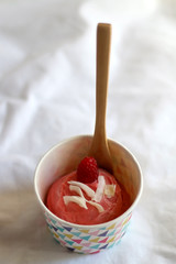 Strawberry vegan ice cream, decorated with raspberry and coconut flakes, in colorful paper cup. Selective focus.