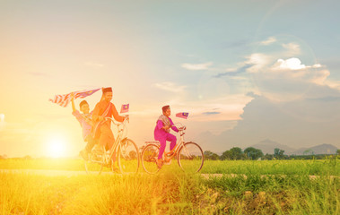 independence Day concept - Two happy young local boy riding old bicycle at paddy field holding a Malaysian flag