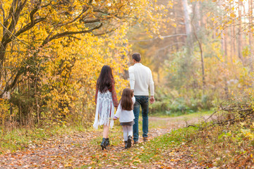 Mom, Dad and Daughter are walking in the autumn forest