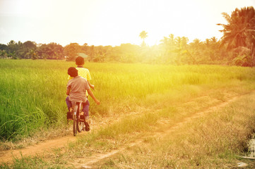 happy young local boy riding old bicycle at paddy field with sunlight