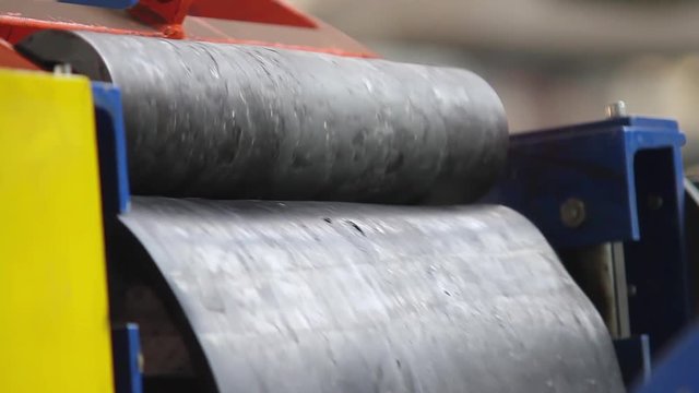 Pressing rubber for tyres production. Rubber tape on a large tire factory close up. Powerful press for the creation of rubber products from rubber. Machine with large shafts kneads rubber compound.