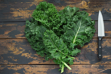 Fresh organic curly kale leaves on a brown wooden table with cook knife, gmo free,  rustic style, free space left side, top view, vignetting - obrazy, fototapety, plakaty