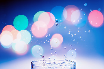 A glass of water with a splash and colorful bokeh glowing. Water - the source of life on the Earth concept