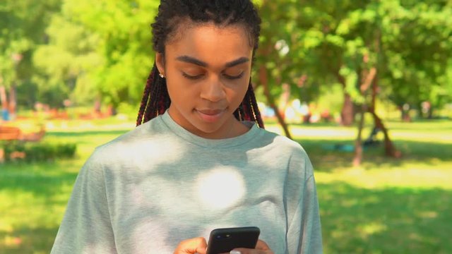 portrait young woman holding smartphone chat online or scrolling social network news feed in summer park