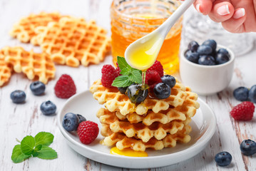 Viennese crispy waffles with fresh berries (raspberries and blueberries) with honey and mint leaves on a white plate on the table. Delicious homemade summer gourmet Breakfast. Selective focus