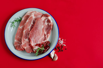 Fresh meat steaks with spices on white plate on red background. Copy space.