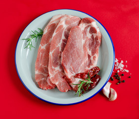 Fresh pork steaks with spices on white plate on red background.
