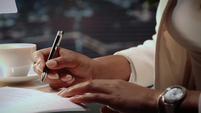 Close up of african american woman's hands signing agreement with pen on the table with a cup of drink