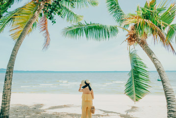 Woman enjoying beach relaxing joyful in summer by tropical blue water. model on travel wearing beach hat.
