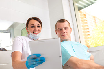 Obraz premium Dentist finishing successful teeth restoration, black haired doctor, in green mask, giving to happy patient mirror, beautiful long-haired woman looking at pristine white teeth with great pleasure