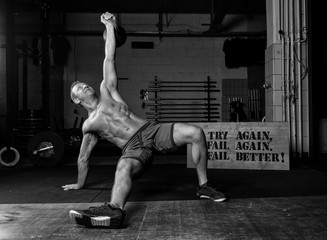 Sportlicher Mann beim Training mit Gewichten. Der hübsche und gebräunte Sportler trainiert oberkörperfrei mit der Kettlebell. Schwarz und weiß.