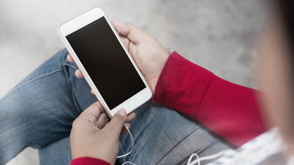 Cropped shot young female using mobile phone and earphones.