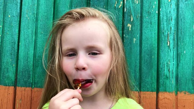 cheerful beautiful little girl eating a lollipop on a green background