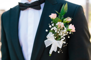 Close-up pink roses boutonniere with the decor on a grooms dark blue elegant jacket, selective focus