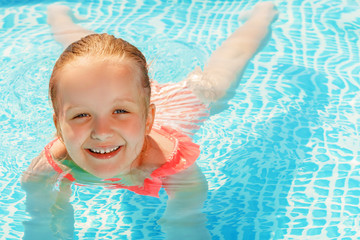 Charming little girl swims in the pool. The child is smiling and looking at the camera.