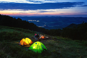 Summer evening in a hike. Glowing tents. Camping in a beautiful location. Sitting around the campfire.	